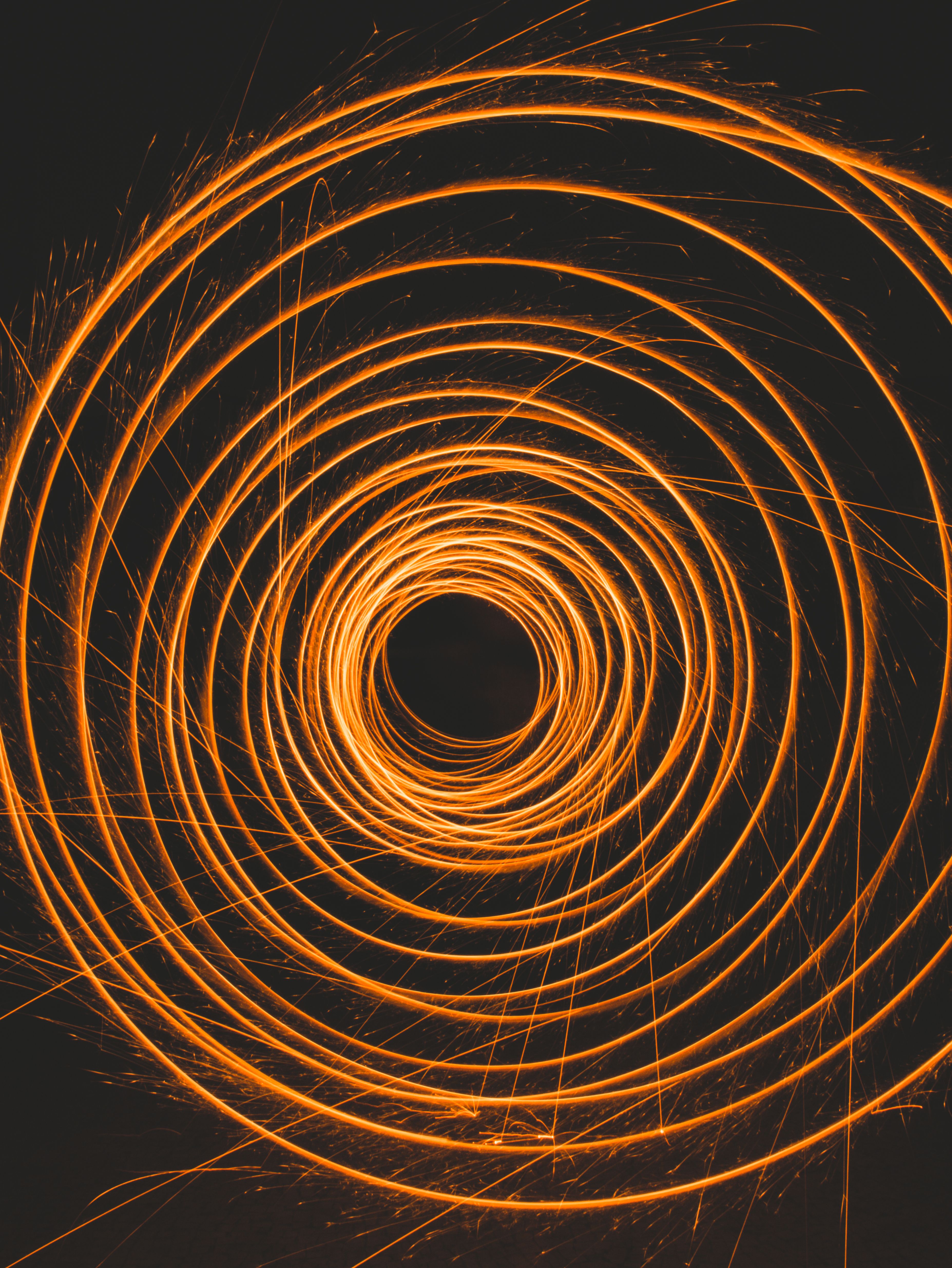 Abstract image of orange spiral light trails against a dark background, resembling swirling fire or sparks.